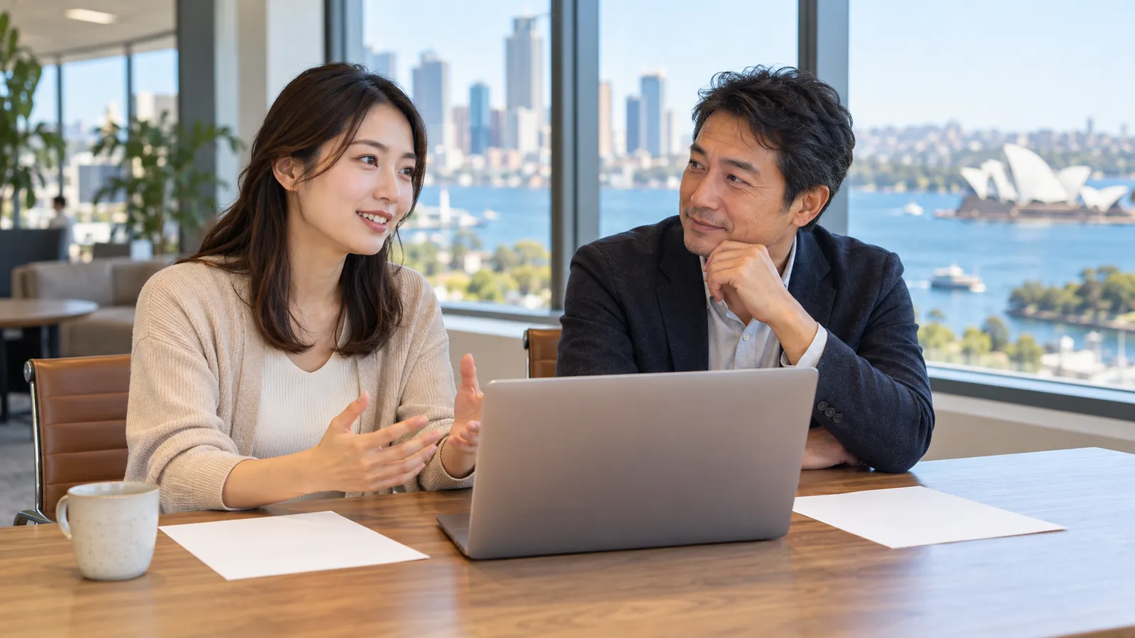 シドニー港を望む明るいオフィスで、ノートパソコンを前に話し合う日本人の男女。